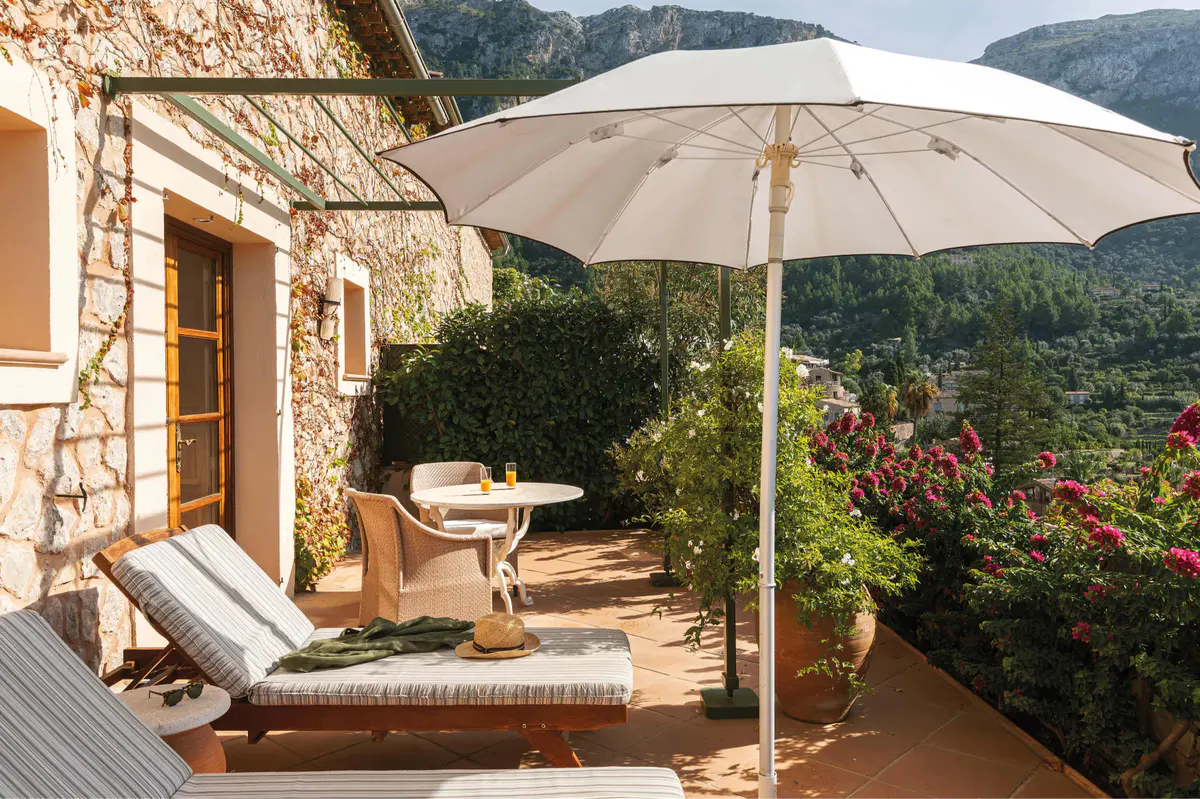 Private terrace with lounge chairs, cream umbrella, and Mediterranean hillside view
