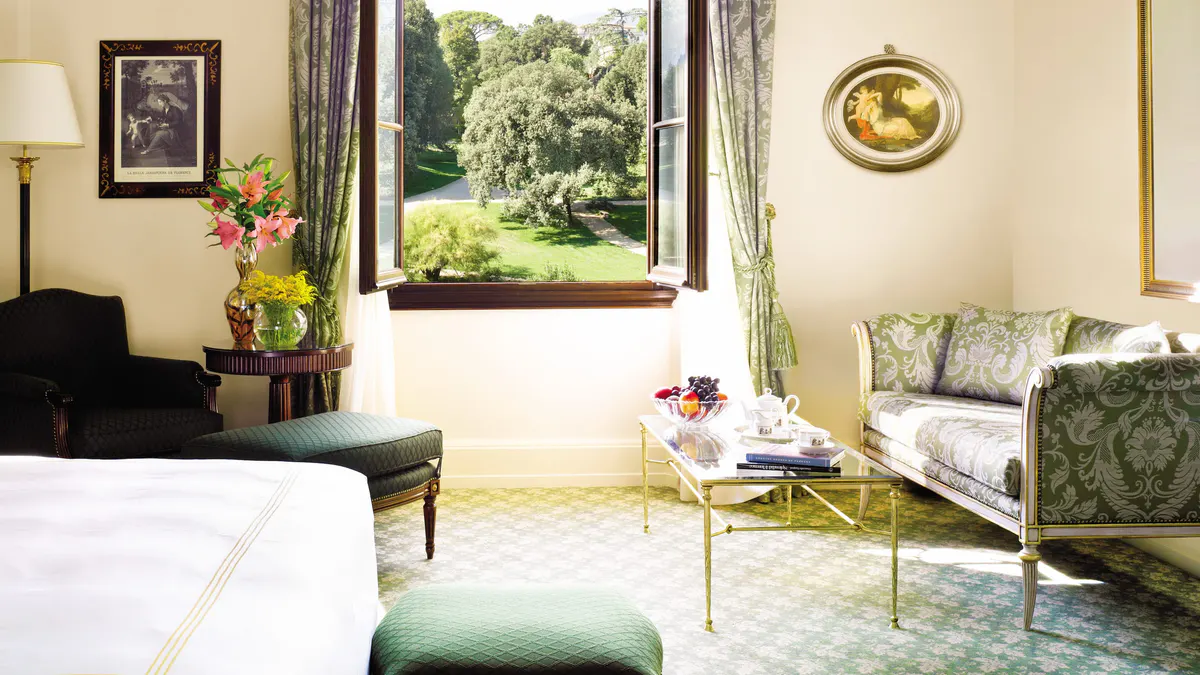 Bedroom with pale walls, garden views through tall windows, and pale green upholstered seating