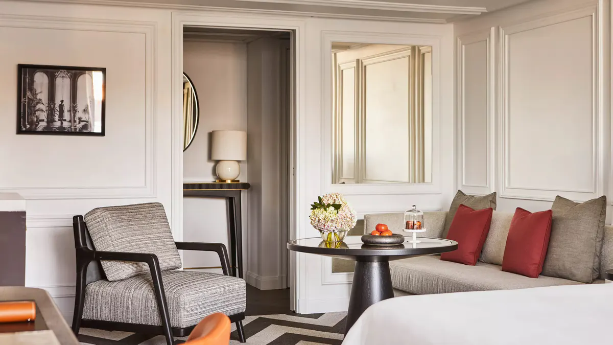 A suite sitting area with accent chairs, marble fireplace, and bedroom beyond