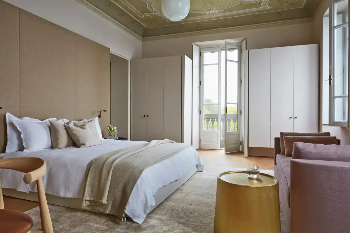 A bright bedroom with beamed ceiling, French doors to a balcony, and lake views