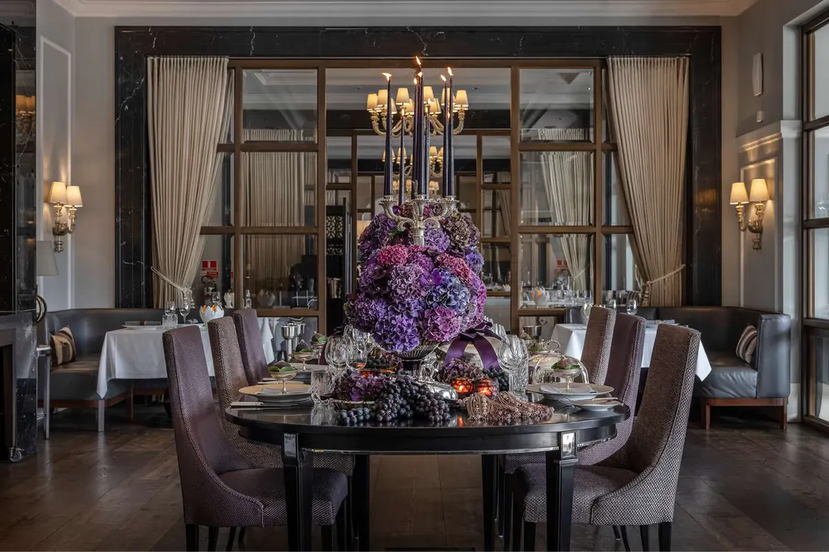 Round dining table with purple floral centerpiece and dark furnishings