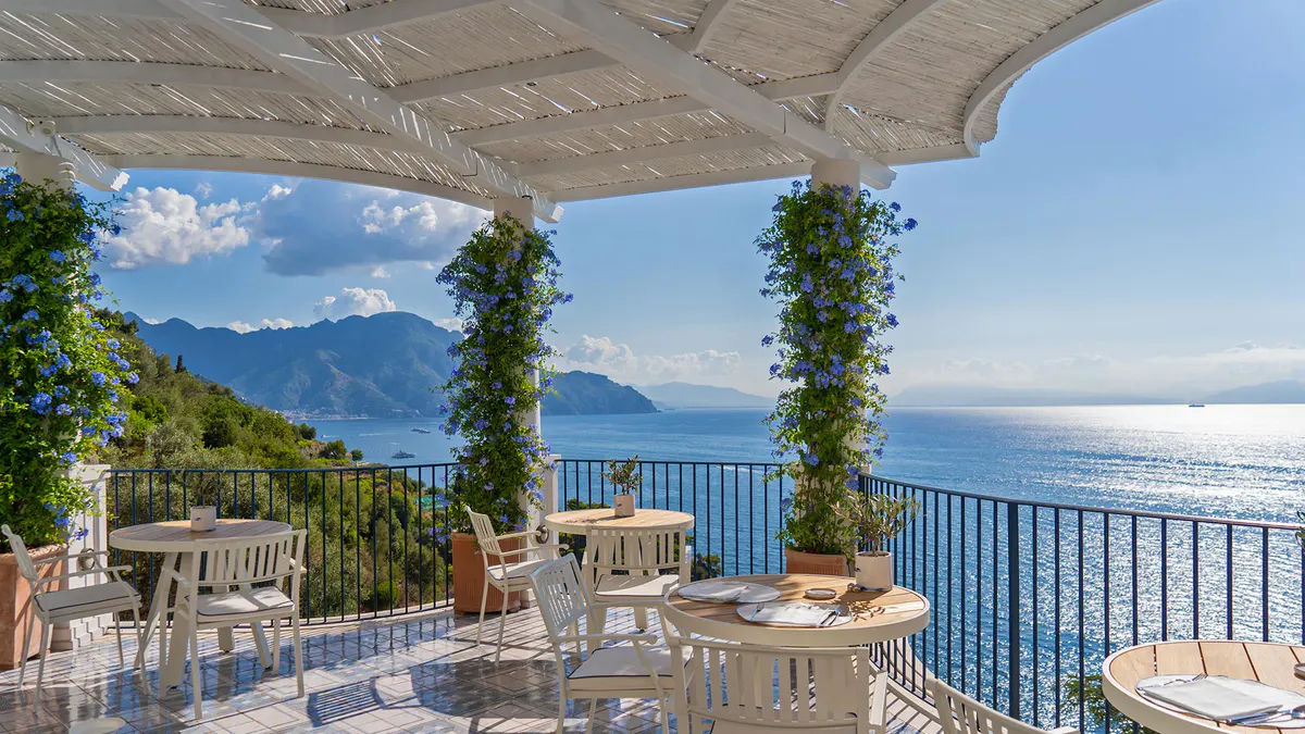Covered dining terrace with ivy-draped columns and unobstructed sea and mountain views