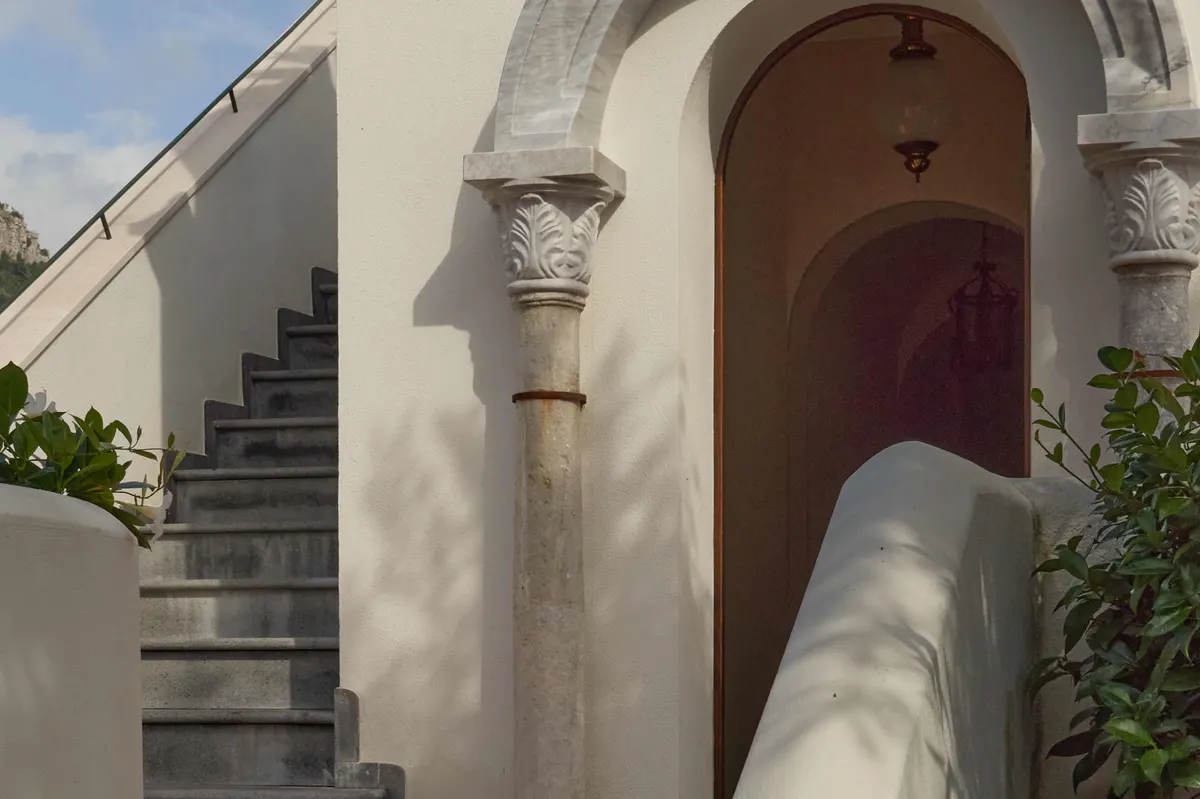 Outdoor archway with ornate column, coastal stairs, and crimson wooden door on whitewashed building