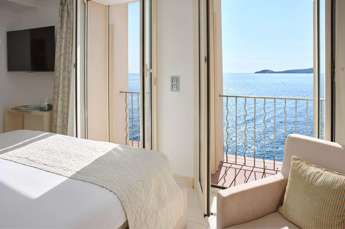 A bedroom with open glass doors to a balcony overlooking blue water