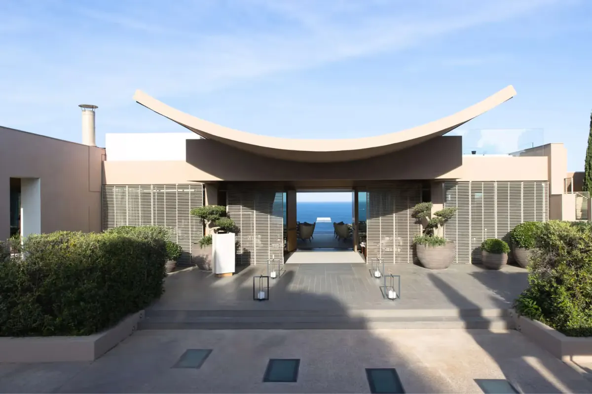 A curved dark pavilion opens onto the Mediterranean Sea and coastline