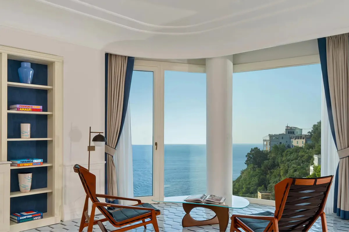 Suite with curved bay windows framing sea views, modern furnishings, and blue-toned decor