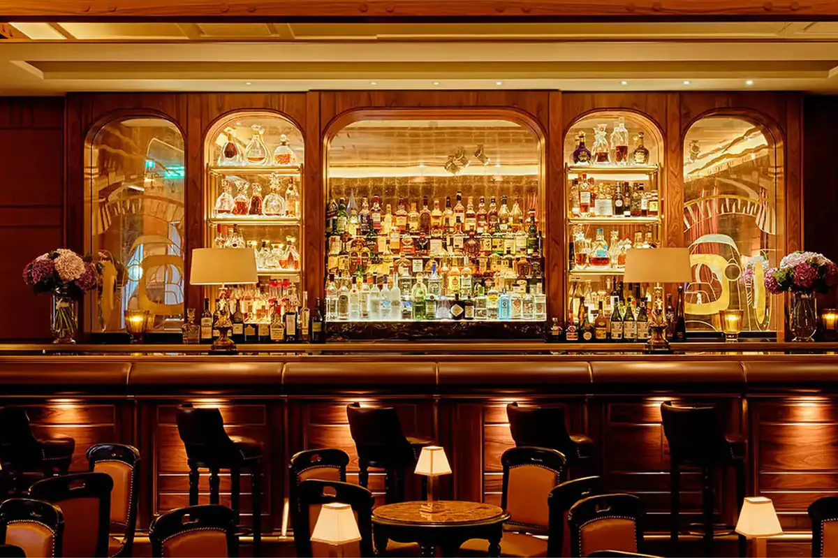 Bar with rich wood paneling, gilt mirrors, and illuminated liquor shelves