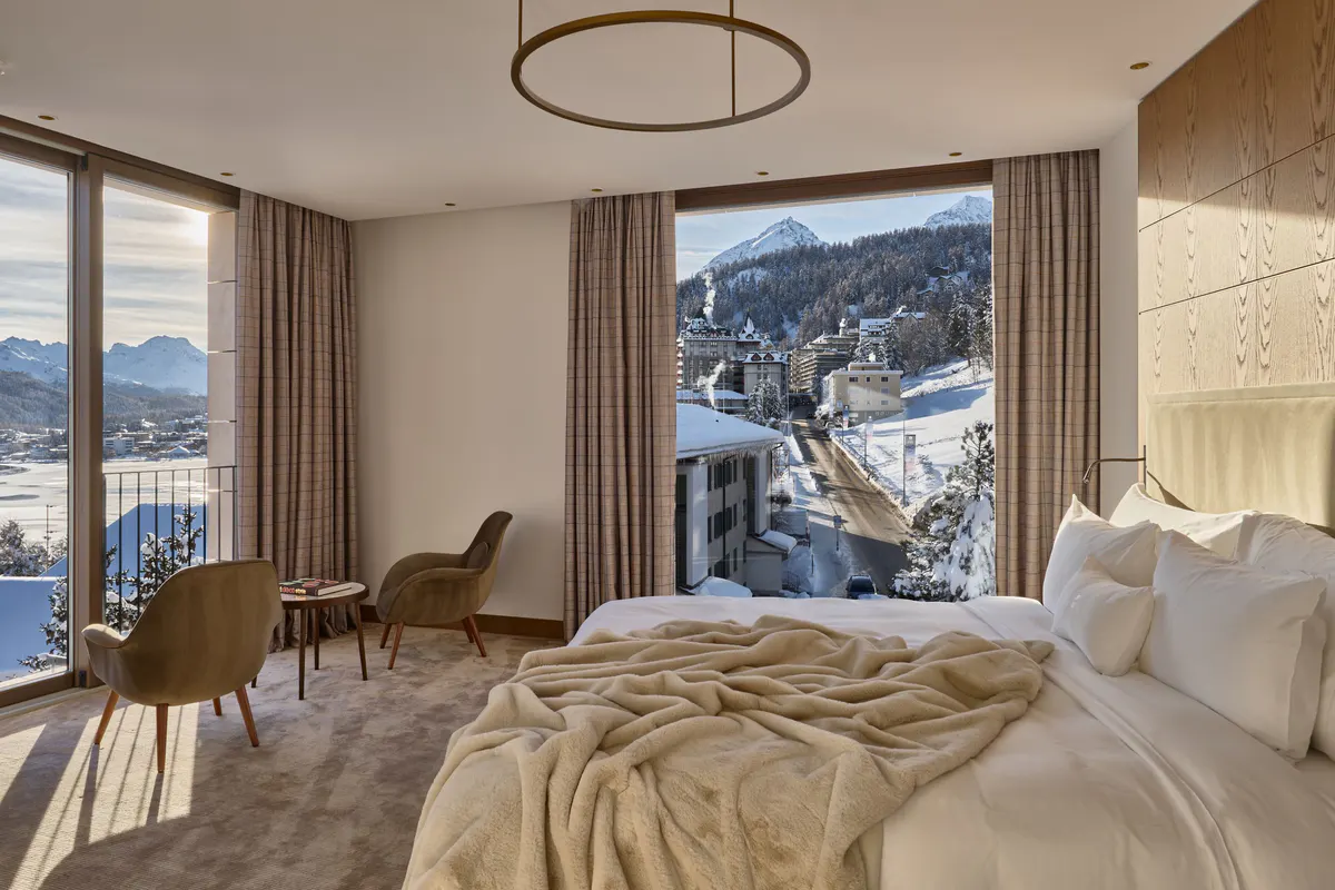 Bedroom with cream bedding, wood furnishings, and floor-to-ceiling windows overlooking mountains