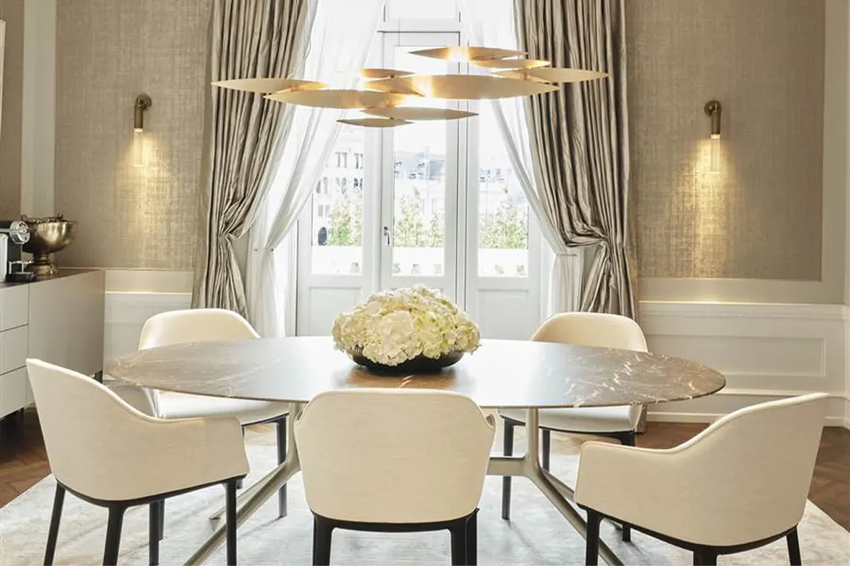Dining room in cream tones with brass chandeliers and tall windows