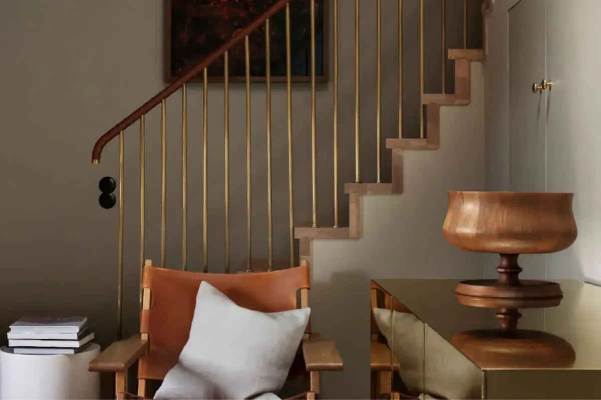 A timber staircase with metal railing next to a bench with cushions and a side table with stacked books