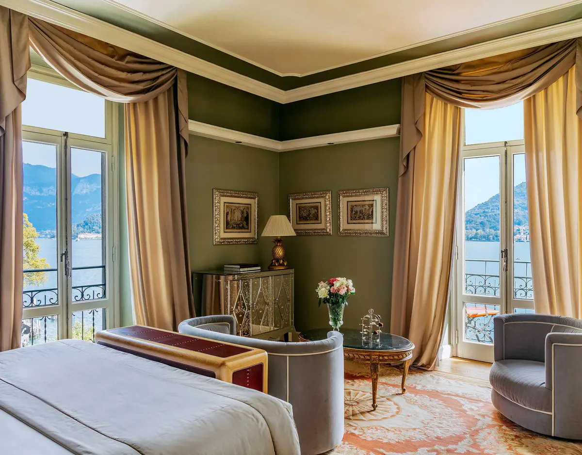 Bedroom with sage-green walls, draped windows, and balcony with distant lake views