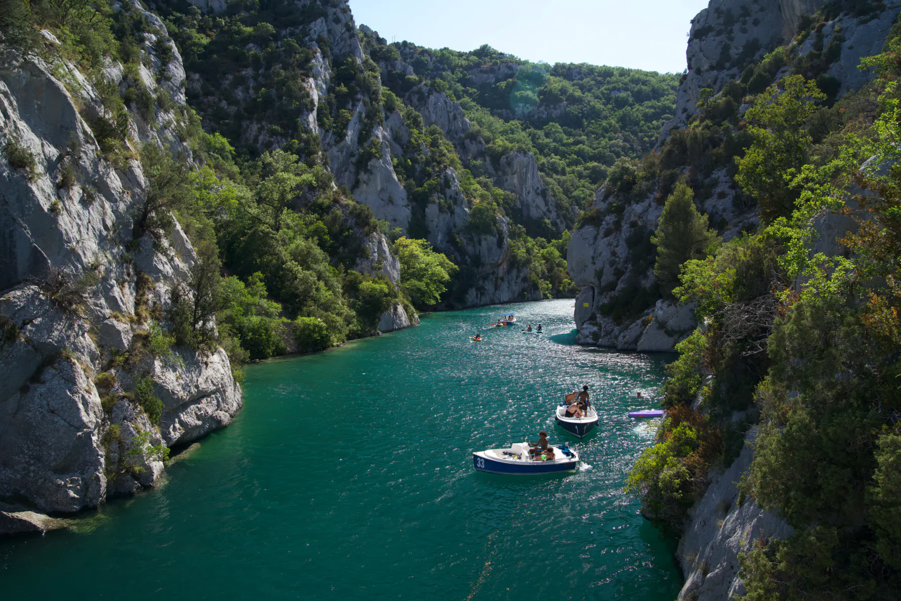 Small boats on the turquoise water of the lower Verdon gorge, between limestone cliffs