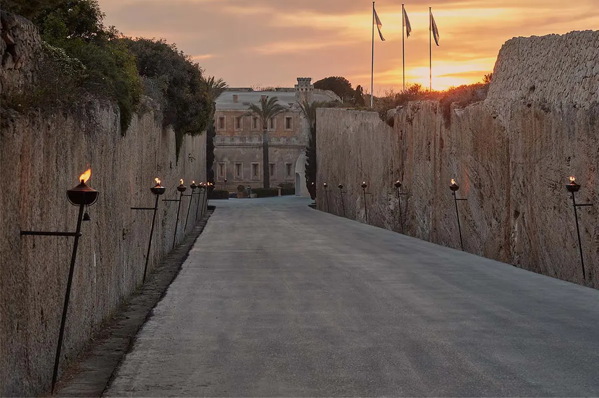 A stone causeway bordered by fortress walls at dusk, leading toward the Mediterranean