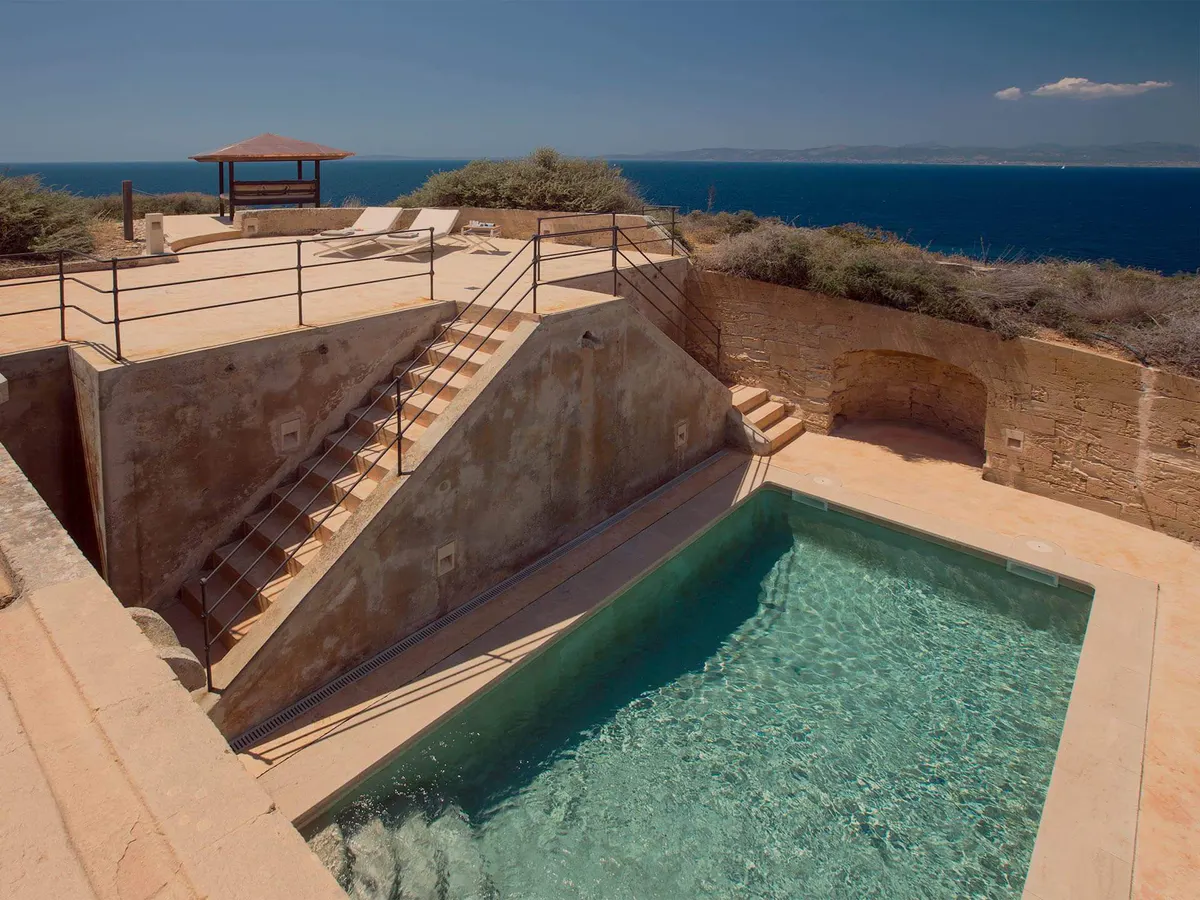 A modern saltwater pool in turquoise waters with railing and coastal rock formations