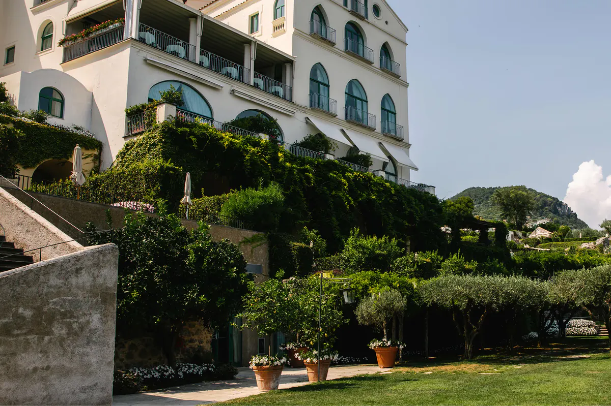 White palazzo exterior with manicured evergreen hedges and terracotta potted plants on sloping lawn