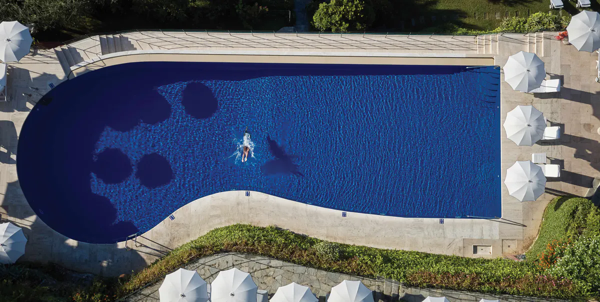 An aerial view of the infinity pool surrounded by white loungers and emerald water