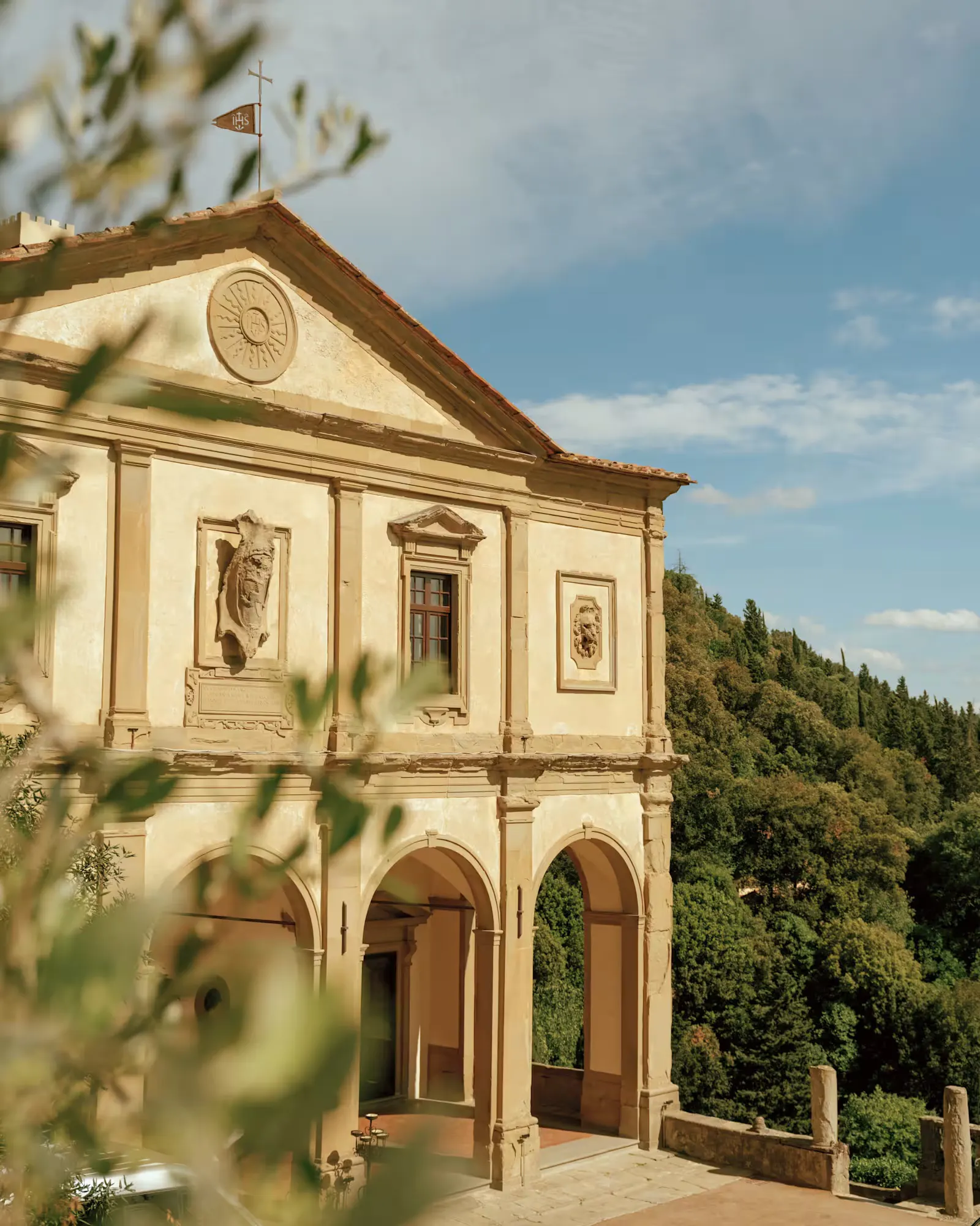 The arcaded facade of Villa San Michele seen through olive branches, with wooded hillside behind