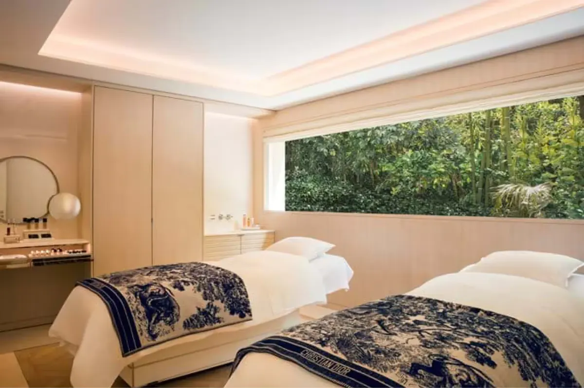 A spa treatment room with white linens, soft ambient lighting, and forest views