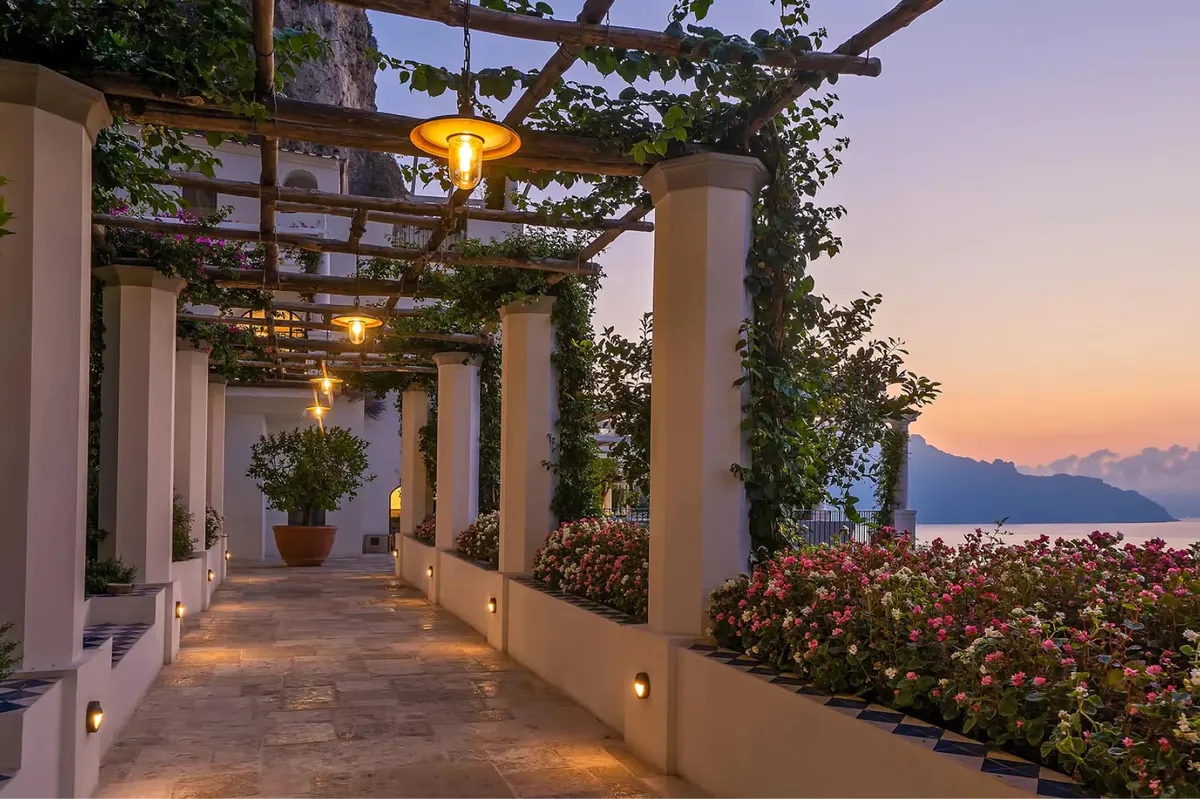 Illuminated pergola pathway at dusk with climbing ivy and sea views in background