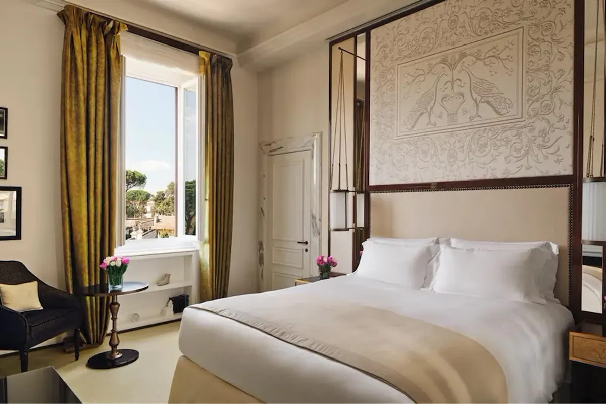 A bedroom with a four-poster canopy bed, window with gold drapes, and pale stone textured walls