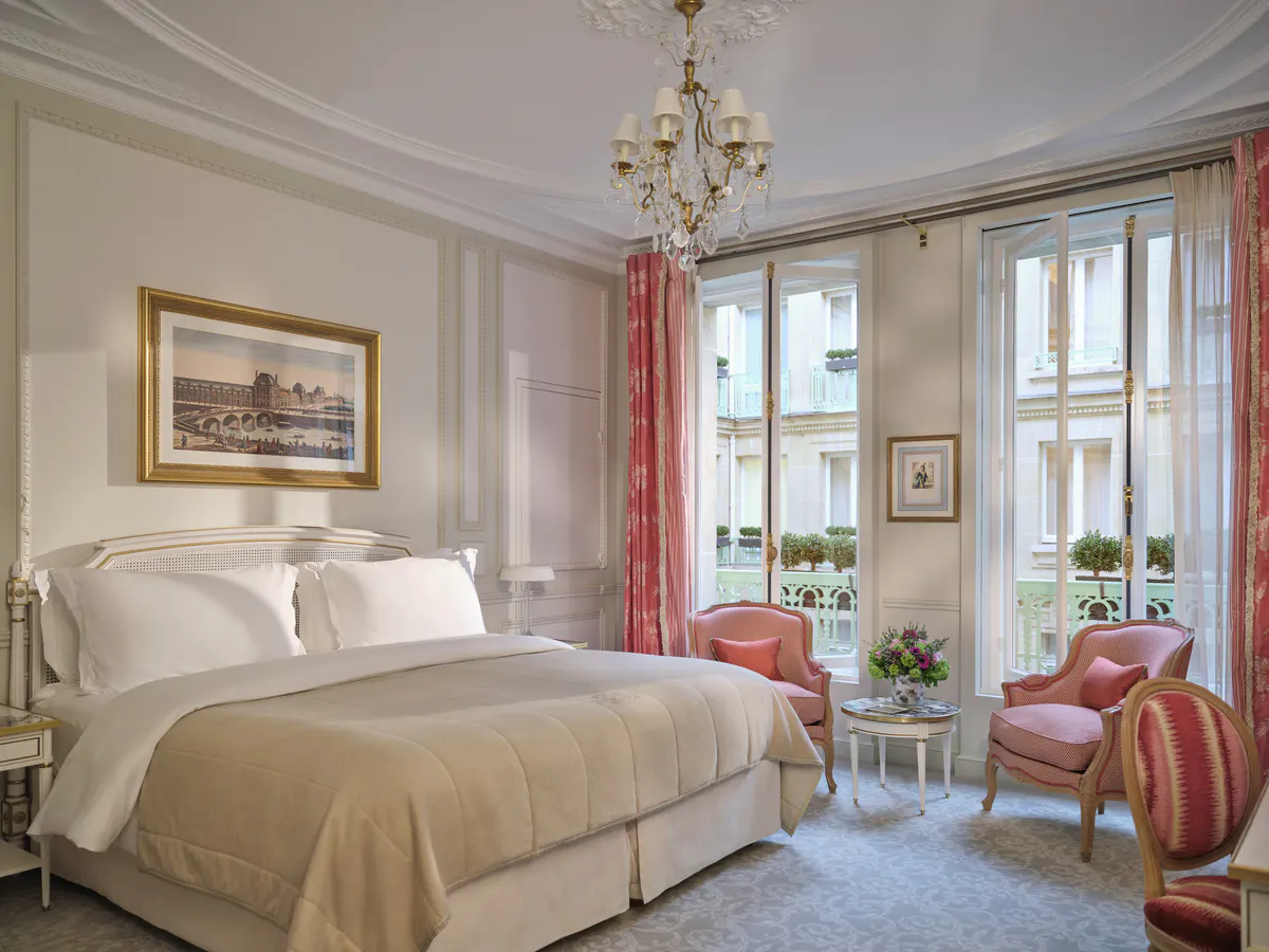 A bedroom with queen bed, cream upholstery, traditional furnishings, and windows with red drapes