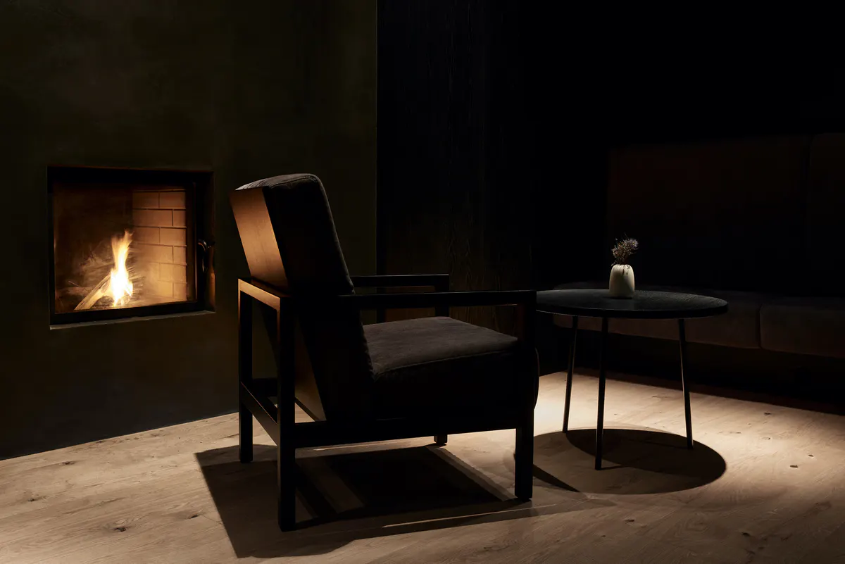 A cozy lounge corner with a modern fireplace insert, wood-frame chair, and soft ambient lighting