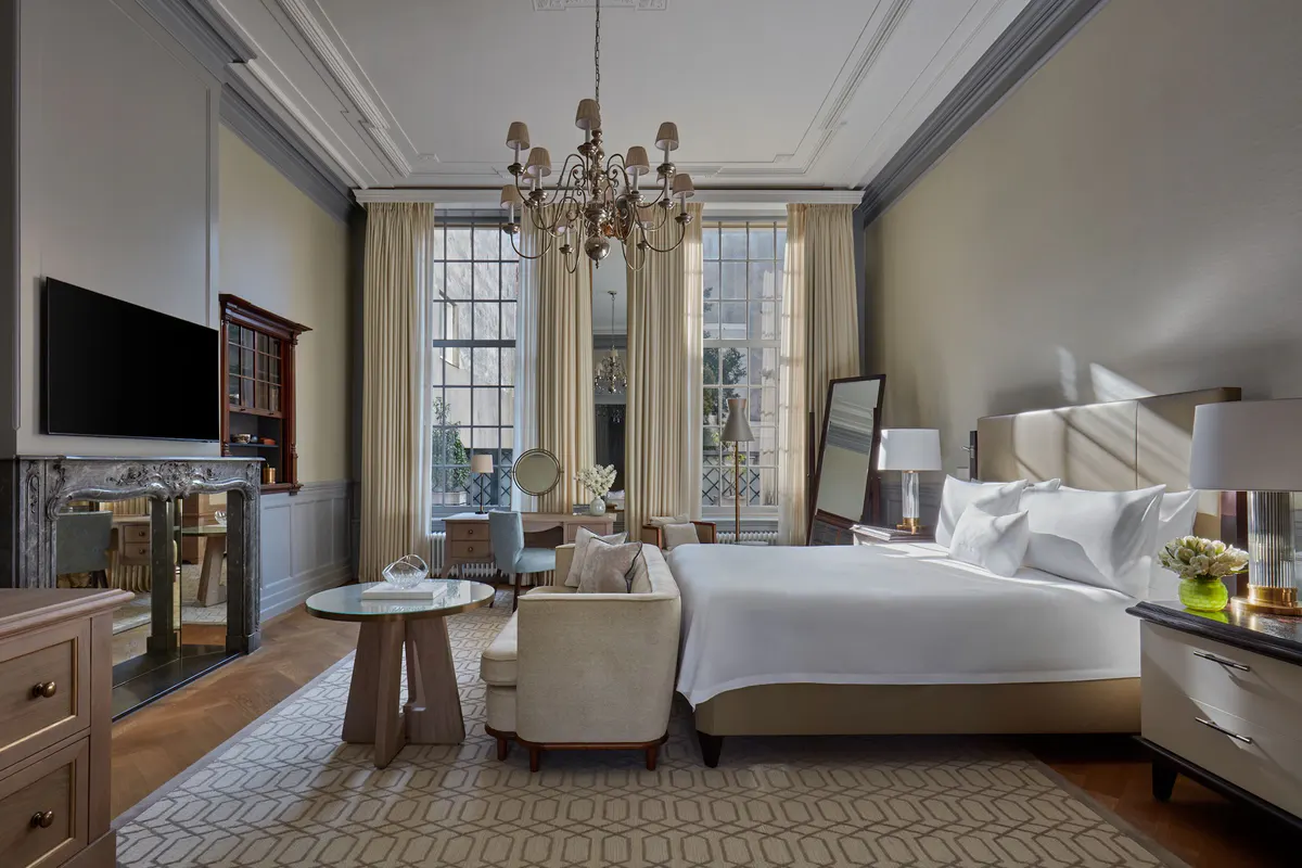 A bedroom with cream paneled walls, high ceilings with cornice details, and windows overlaid with ornate frames