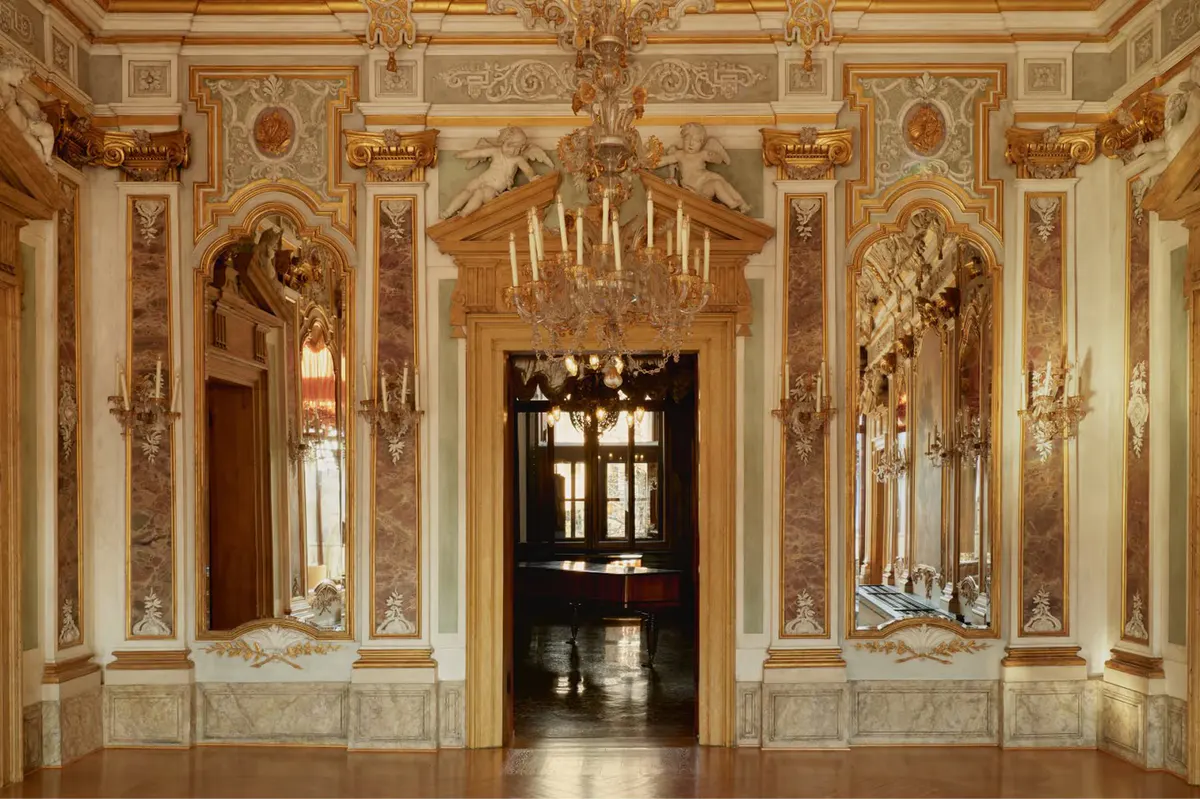 A neoclassical gallery with cream and gold painted walls, arched alcoves, and ornamental details