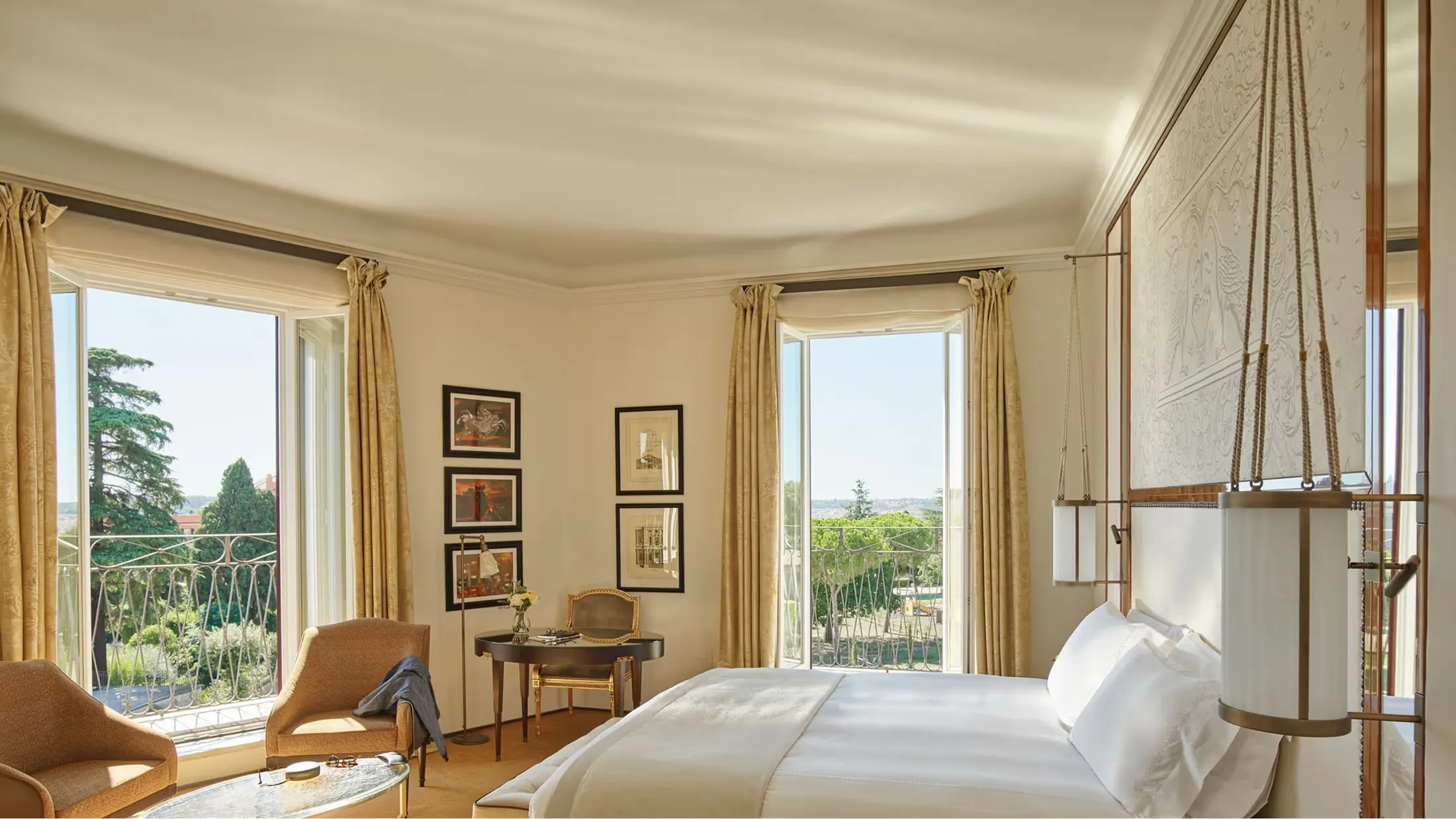 A bedroom with pale stone walls, tall windows overlooking Rome, and natural light illuminating the bed