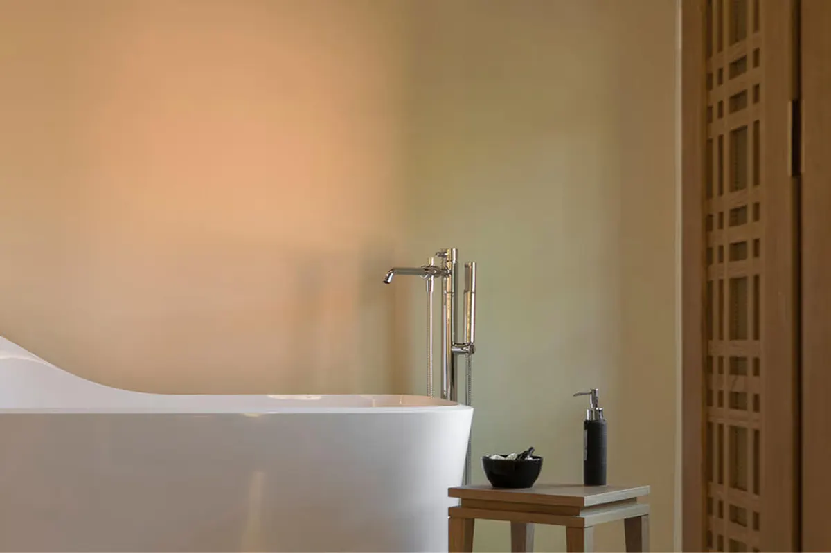 A soaking tub with warm ambient lighting beside a wooden shelf