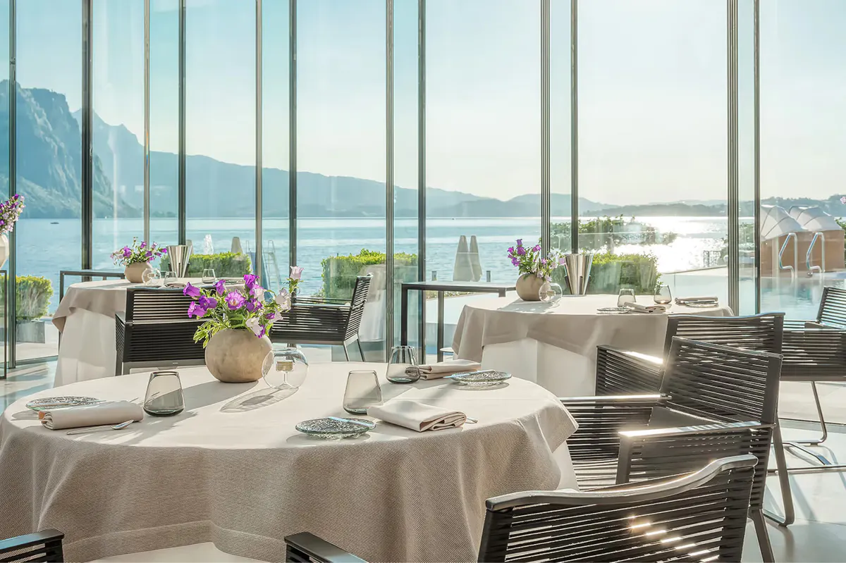 Dining room with round tables, floor-to-ceiling windows framing the lake