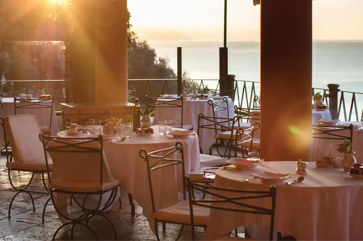 An elegant outdoor dining room with table settings and ocean view at sunset