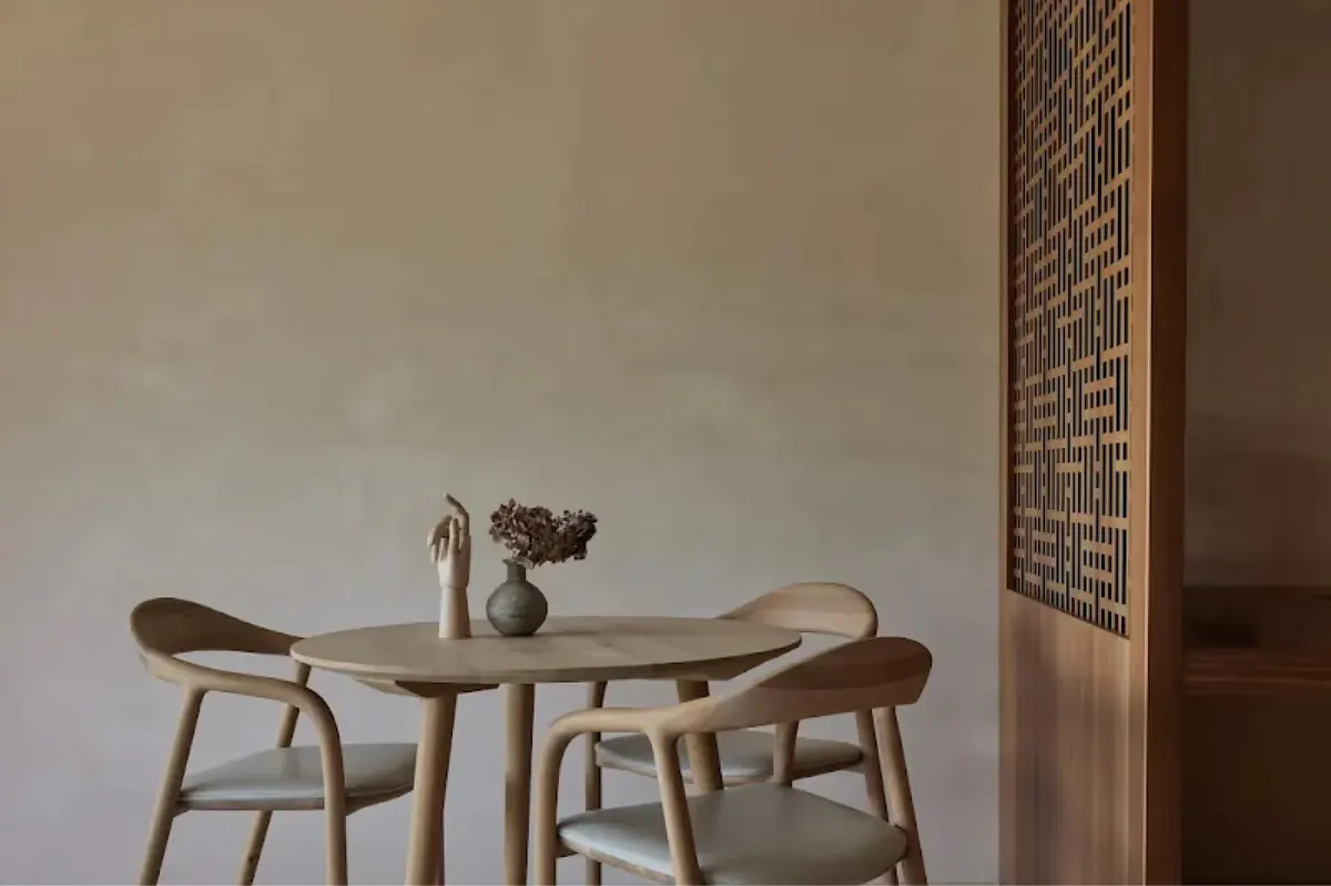 Minimal dining table with two wooden chairs beside an informational board on neutral walls