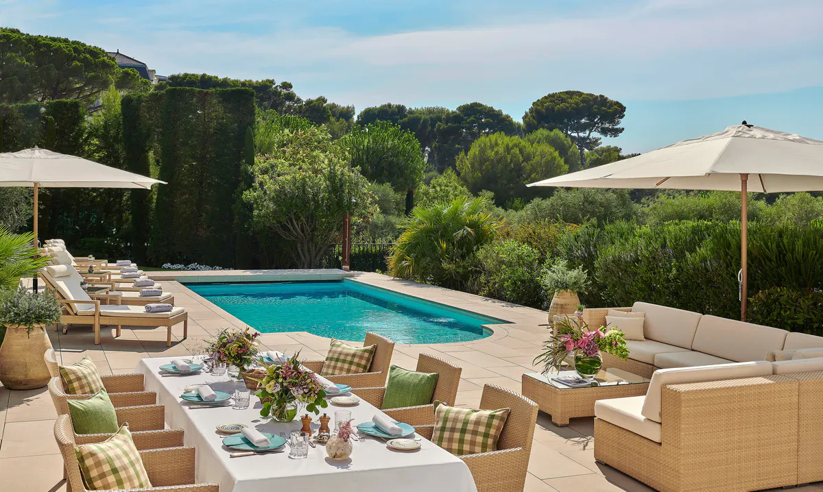 A waterfront terrace with loungers, daybeds, and a view of turquoise water and distant coastline