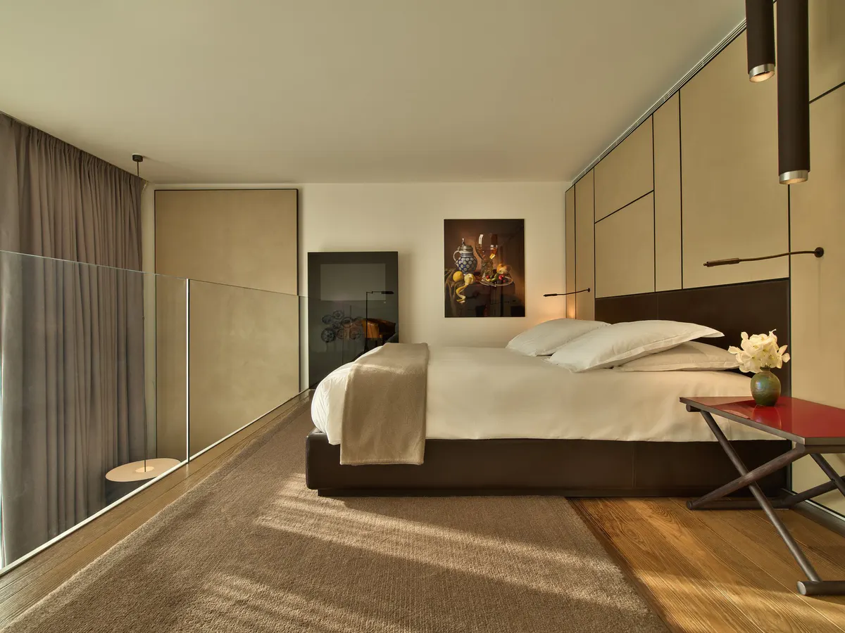 Minimalist bedroom with a charcoal bed frame, cream linens, and floor-to-ceiling windows with curtains