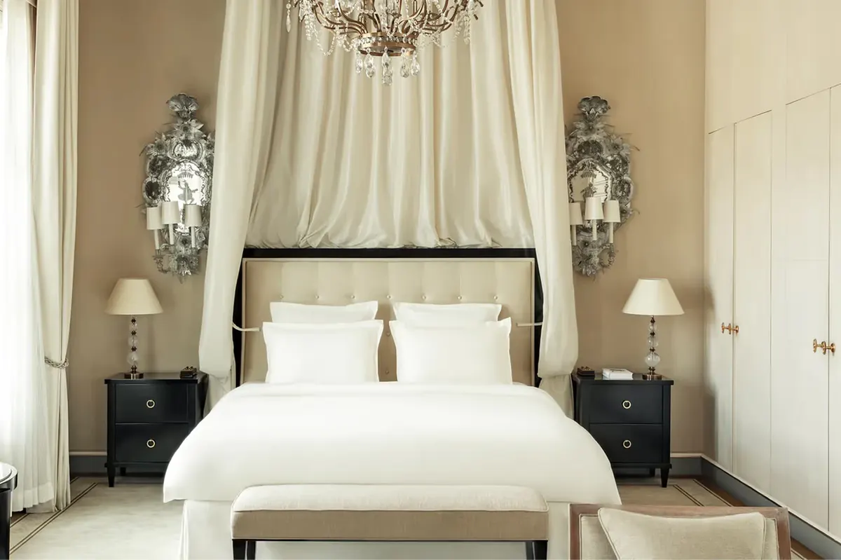 A bedroom with sheer curtains, cove ceiling details, crystal chandelier, and black platform bed