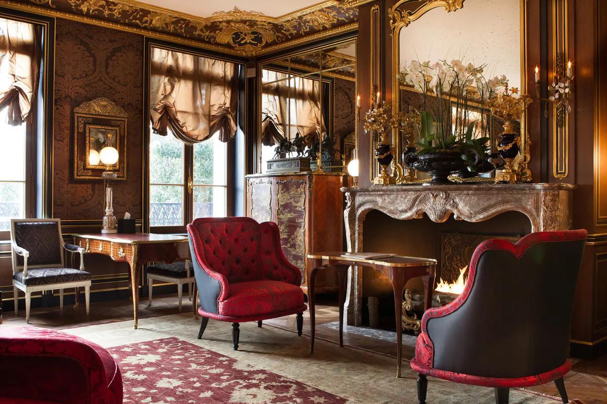 A living room with cream and gold molding, burgundy furniture, and marble fireplace