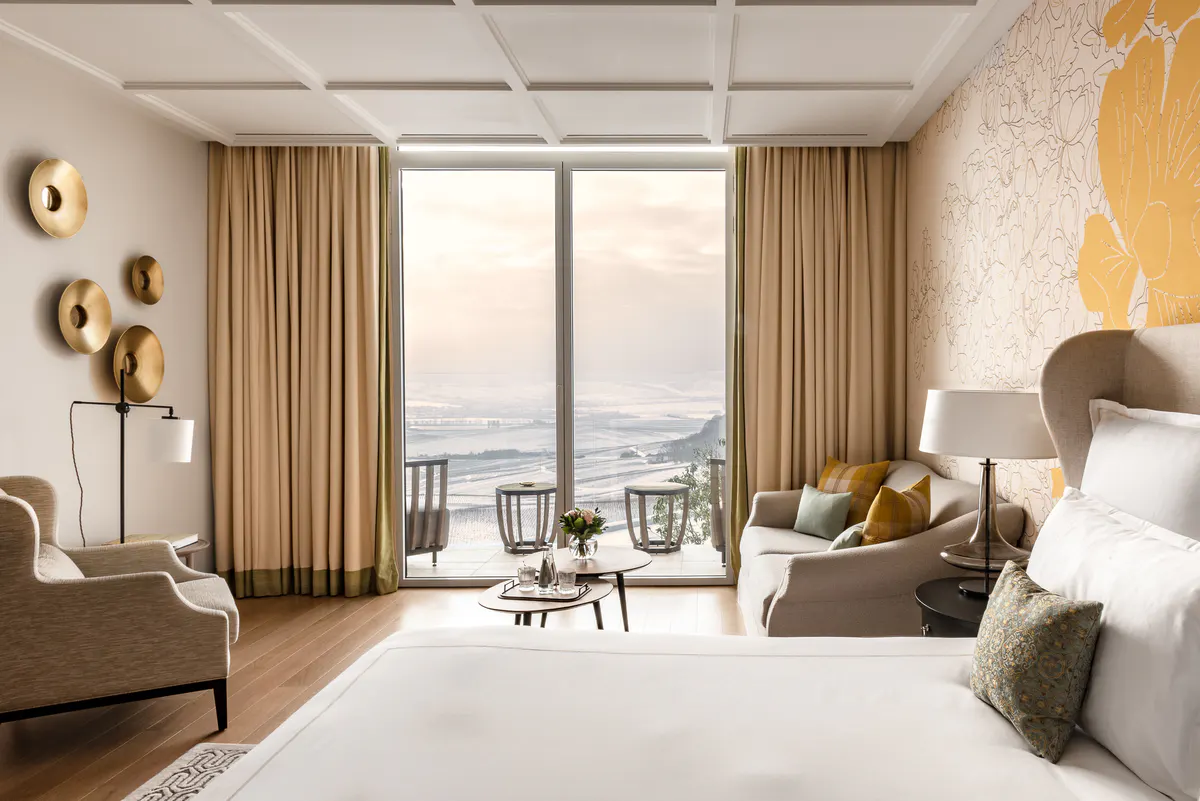 Bedroom with mustard accents, natural wood details, and glass doors framing water views