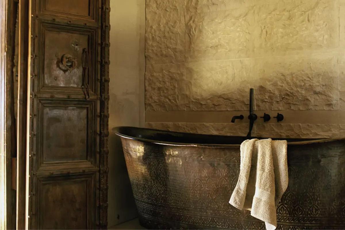 Stone bathroom with antiqued metal freestanding tub and weathered plaster walls
