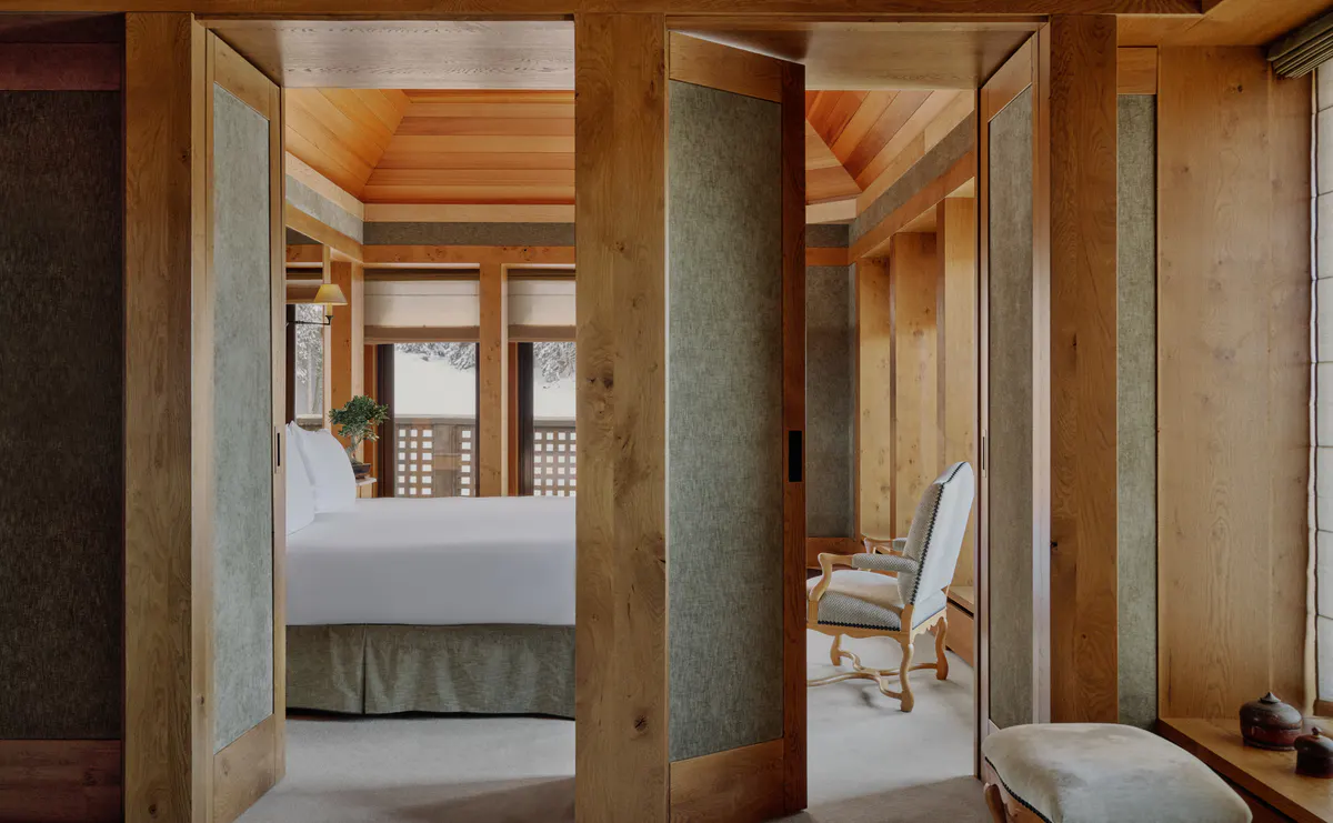 Suite viewed through open wood doors, with a bed and lattice screened window beyond