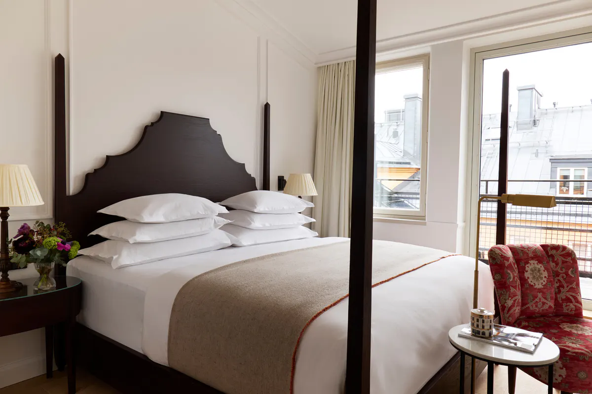 Guest bedroom with dark canopy bed, white linens, and windows with city views