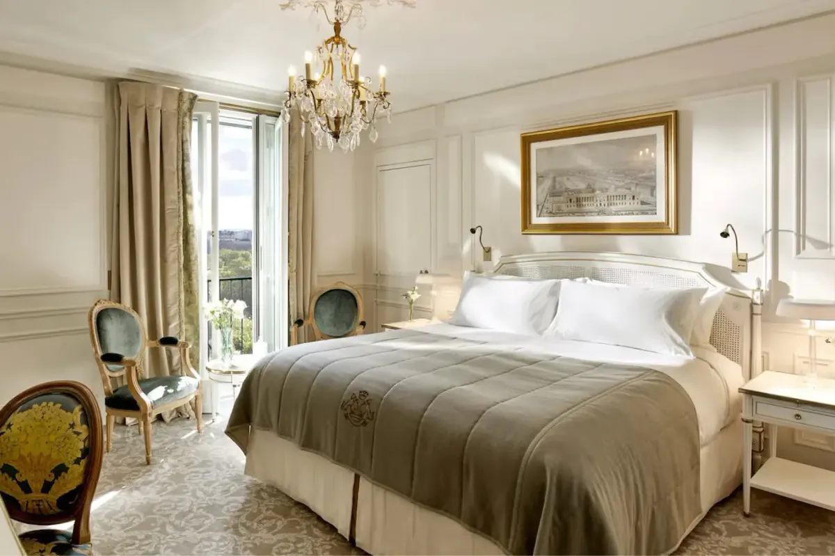 A bedroom with bed dressed in neutral linens, framed artwork, and floor-to-ceiling windows