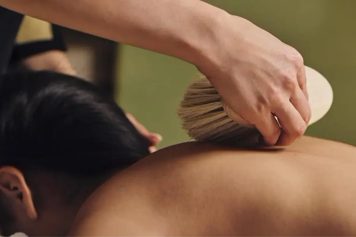 Hands applying a spa massage treatment with a wooden brush on a person’s back
