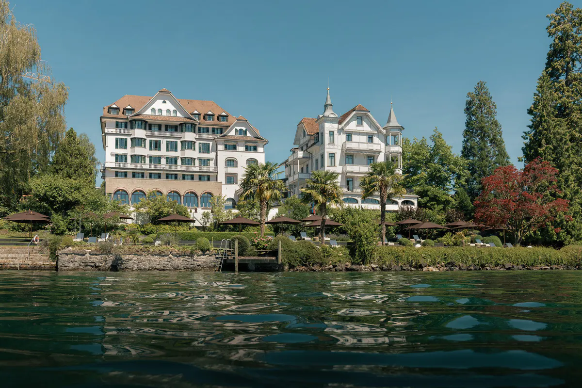 Hotel building complex seen from Lake Lucerne waterside, green grounds and manicured landscaping