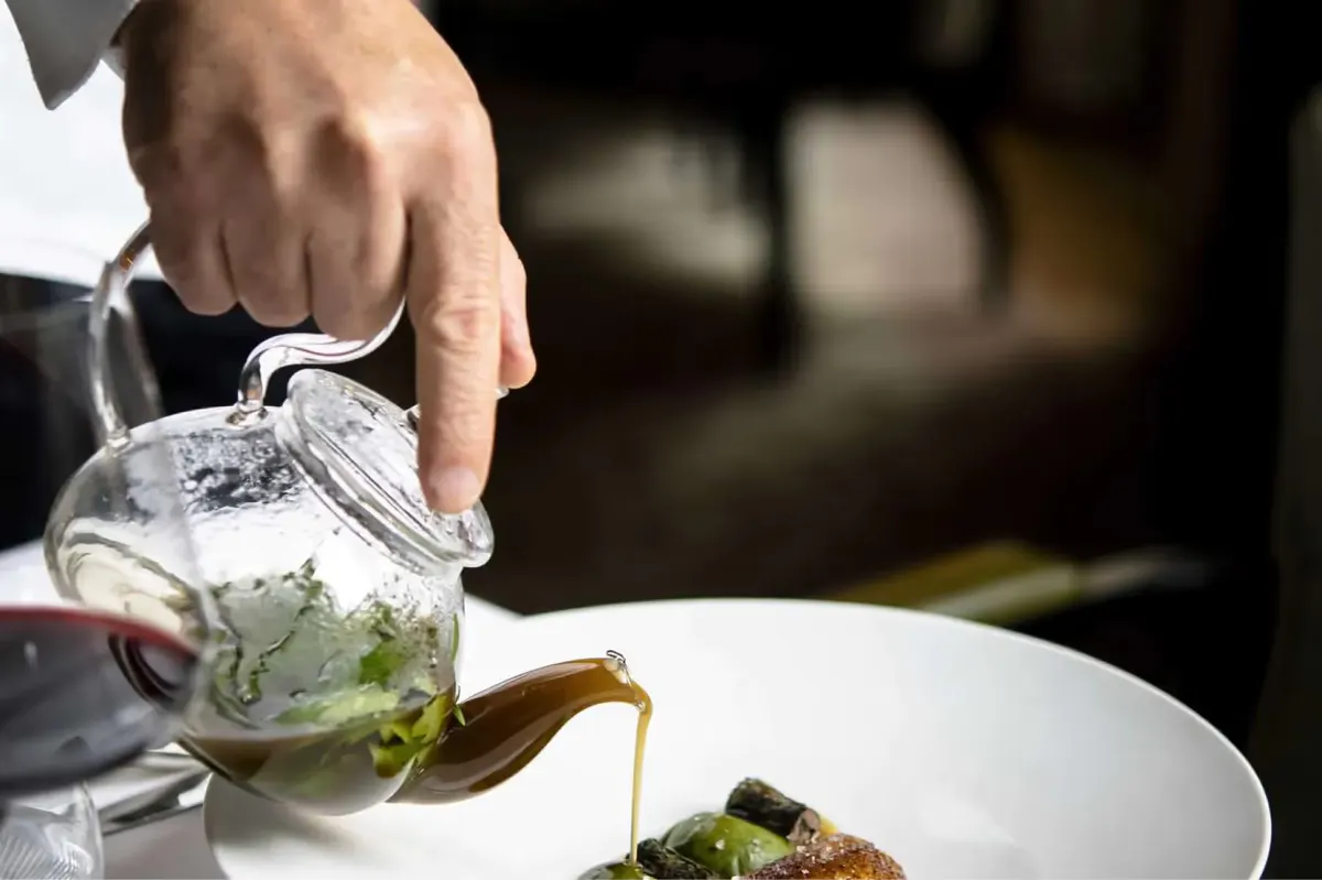 A server pouring dressing over a salad plate with precision