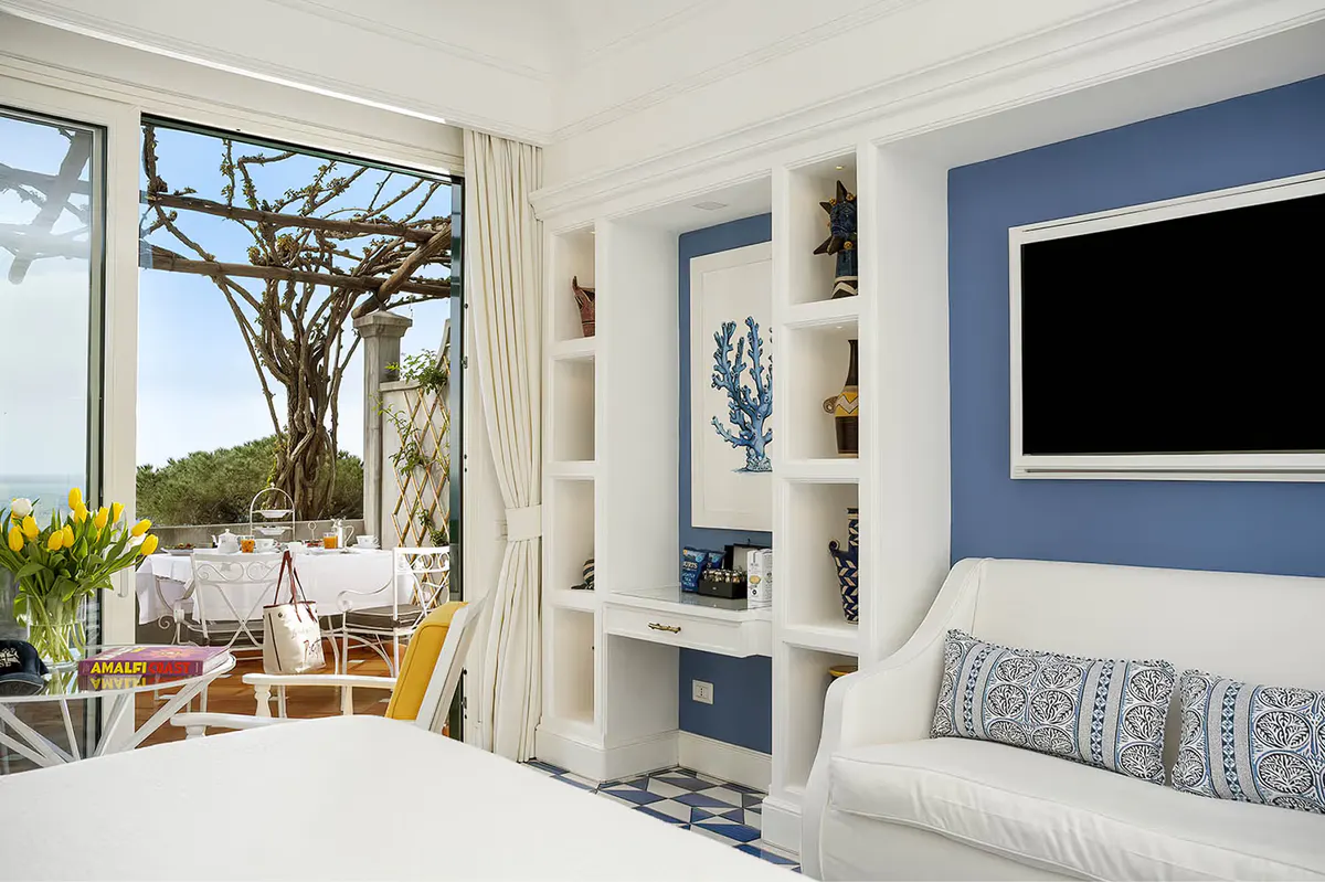Bedroom with white linens, built-in shelving, floor-to-ceiling windows, sea view terrace, and blue accent wall