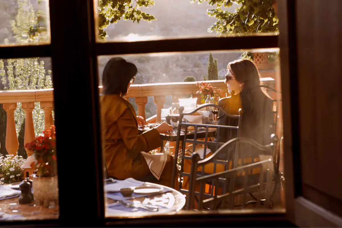 Two diners visible through window frame of restaurant with landscape view beyond