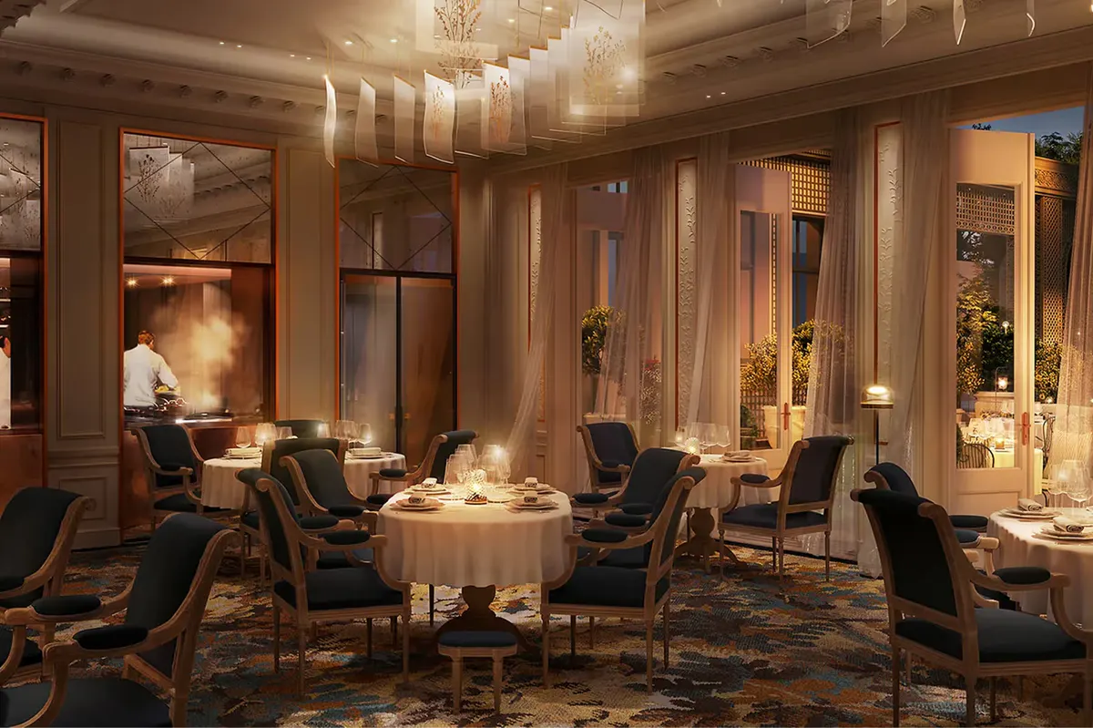 An upscale dining room with gold sconces, round table settings, and dark wood ceiling