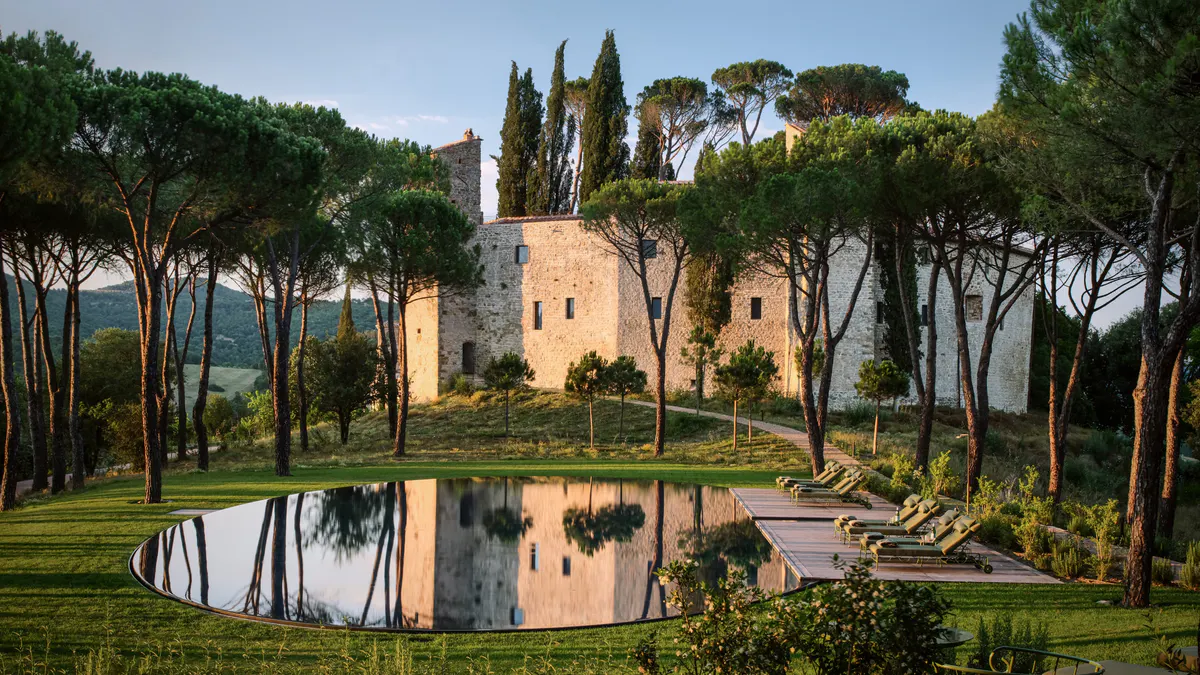 The castle rising above pine trees, reflected in an oval pool cut into the lawn below