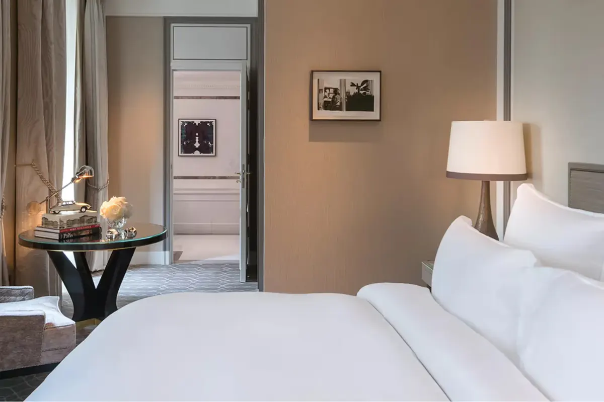 Neutral toned bedroom with round table, white bedding, and tan walls